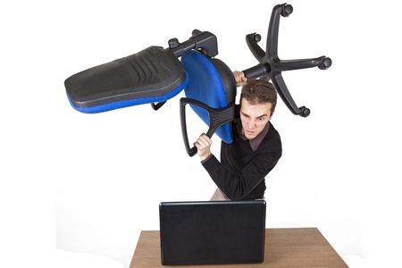 young angry man standing above a laptop with an office chair preparing to destroy itの写真素材