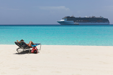 young woman in chair on a beach with cruise ship in the backgroundの写真素材