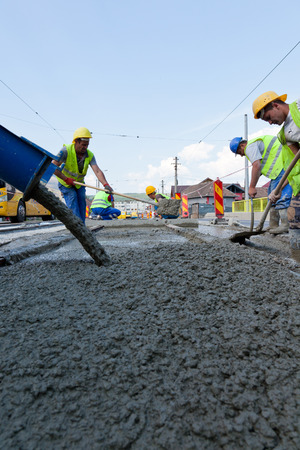 construction team pouring concrete on a road with boots and protection gearのeditorial素材