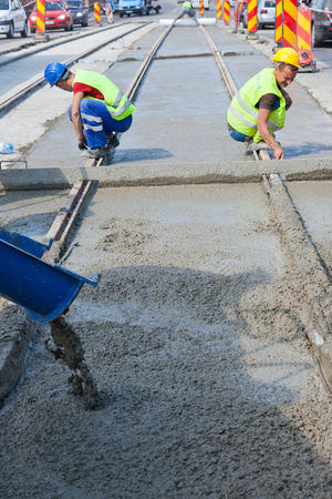 construction team pouring concrete on a road with boots and protection gearのeditorial素材