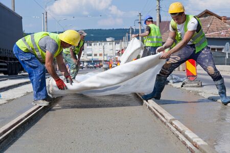 construction team pouring concrete on a road with boots and protection gearのeditorial素材