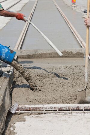 construction team pouring concrete on a road with boots and protection gearのeditorial素材