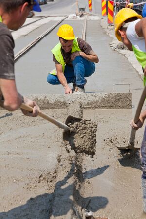 construction team pouring concrete on a road with boots and protection gearのeditorial素材