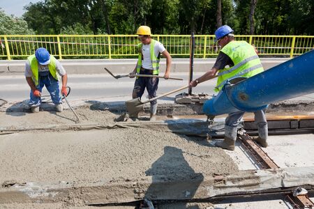 construction team pouring concrete on a road with boots and protection gearのeditorial素材