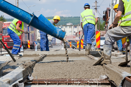 construction team pouring concrete on a road with boots and protection gearのeditorial素材