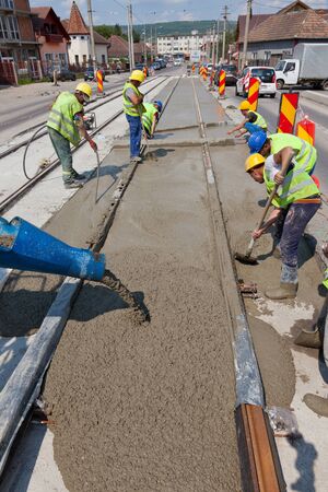 construction team pouring concrete on a road with boots and protection gearのeditorial素材