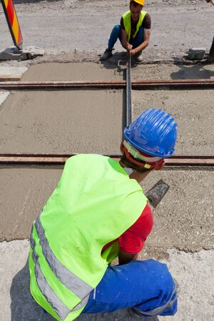 construction team pouring concrete on a road with boots and protection gearのeditorial素材