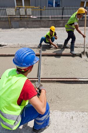 construction team pouring concrete on a road with boots and protection gearのeditorial素材