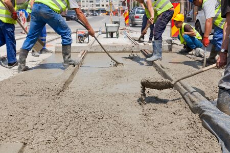 construction team pouring concrete on a road with boots and protection gearのeditorial素材
