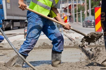 construction team pouring concrete on a road with boots and protection gearのeditorial素材