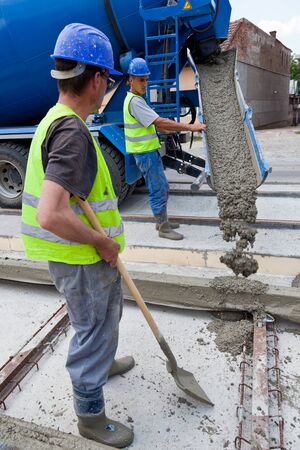 construction team pouring concrete on a road with boots and protection gearのeditorial素材