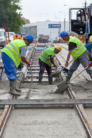 construction team pouring concrete on a road with boots and protection gearのeditorial素材