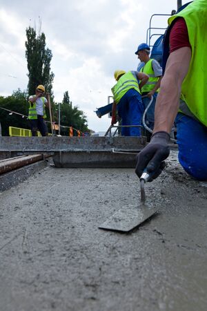 construction team pouring concrete on a road with boots and protection gearのeditorial素材