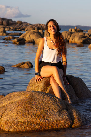 woman sitting on a rock in the ocean on the beach at sunset smillngの写真素材