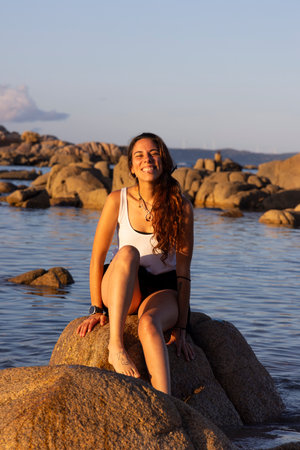 woman sitting on a rock in the ocean on the beach at sunset smillngの写真素材