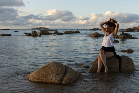 Young Galician woman on the seaside sitting on a rock at sunset near the oceanの写真素材