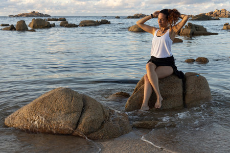 Young Galician woman on the seaside sitting on a rock at sunset near the oceanの写真素材