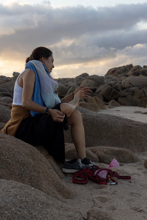 Young woman sitting on rocks on the beach at sunset smilling.の写真素材