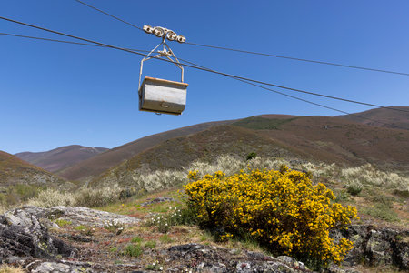 Coal mining cart on rope way cable way abandoned industrial equipment in the mountains on a clear sunny day with blue sky and spring flower meadow.の写真素材