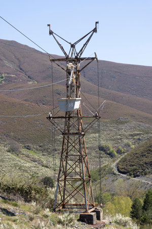 Abandoned industrial coal mining cart on cableway with rusty metal tower with cable on a bright sunny spring day with flower meadow and blue skyの写真素材