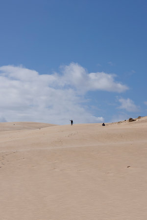 People trekking on foot walking up sand dune on a bright sunny day with blue sky at Punta Paloma in the south of Spain.の写真素材