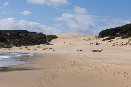 Old abandoned boat on the sand beach next to ocean with people walking on a bright sunny day with blue sky.の写真素材