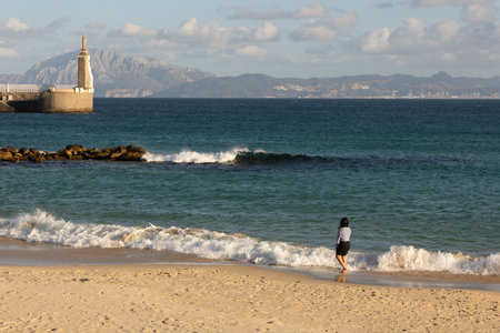 Tourists on the beach at statue of Jesus in Tarifa harbor on a bright sunny day with clouds.の写真素材