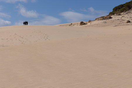 Arid sand dunes in summer with tourist walking up in Punta Paloma on a bright sunny day with blue sky and coulds.の写真素材