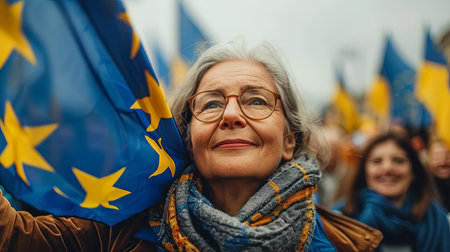 Close-up portrait of happy elderly woman with a smile holding eu blue flag with yellow stars outdoors for european parliament electionsの素材