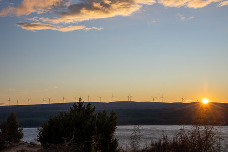 Wind turbines stand proudly against a stunning sunset, symbolizing renewable energy and hope for a sustainable future, set in a picturesque landscape of rolling hills.の写真素材