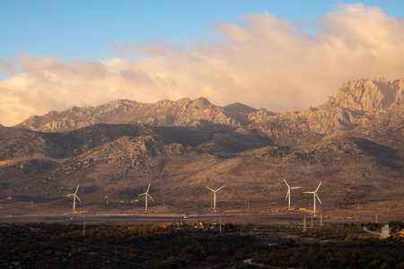 This stunning image showcases several wind turbines set against a backdrop of rugged mountains, highlighting the harmony between renewable energy and nature's beauty.の写真素材
