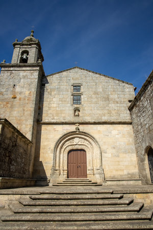 This image captures a charming stone church facade with detailed carvings, showcasing Romanesque architecture and its grandeur against a bright blue sky.の写真素材