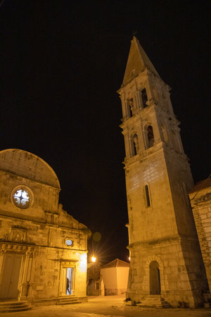 The illuminated historical church tower stands majestically at night, showcasing its architectural details. The warm light adds charm to the dark, tranquil surroundings.の写真素材