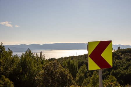 A coastal view showcasing sparkling water under sunlight along with a nearby warning traffic sign,...