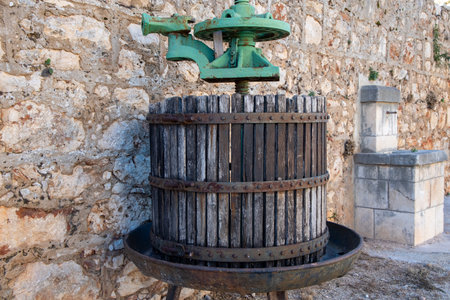 An old vintage press with a green handle positioned next to a stone wall, depicting a blend of rustic technology and historical architecture in a serene setting.の写真素材