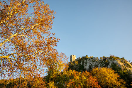 A stunning view of a medieval castle perched atop a rocky hill, surrounded by vibrant autumn foliage, capturing the essence of nature's beauty during fall.の写真素材