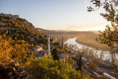 A picturesque scene showcasing an autumn landscape with a river winding through hills, featuring historical structures, colorful foliage, and a serene environment.の写真素材