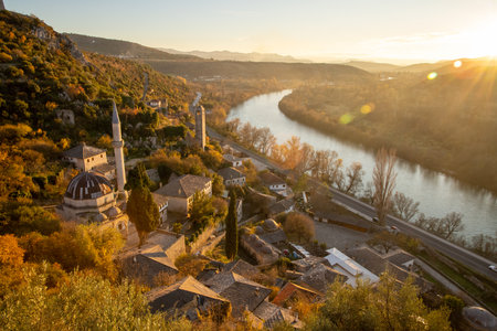 A breathtaking view of a picturesque village alongside a winding river, framed by lush hills, illuminated by the warm light of the setting sun at golden hour.の写真素材