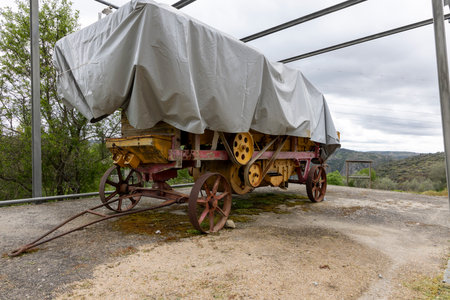An inclined view of an old farm wagon covered by a tarp under a metal structure, evoking rural lifestyle and historical agriculture.の写真素材