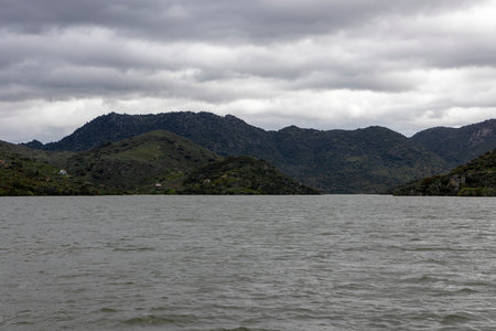 Expansive view of a calm lake flanked by verdant hills under a moody, overcast sky, offering a sense of tranquility and natural beauty.の写真素材