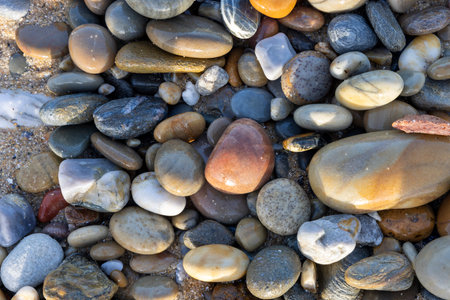 High-angle, close-up view of a collection of smooth, rounded sea stones of varying sizes and colors....