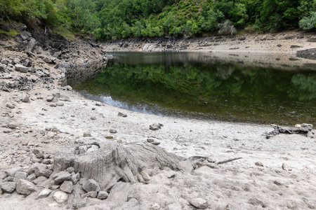 The image presents a high-angle, medium shot of a small, secluded waterhole nestled within a rocky landscape. The water is still and reflective, exhibiting a dark greenish hue.の写真素材