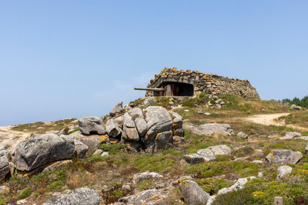 A rocky hill with a small building on top. The building is made of stone and has a cannon on top. The hill is surrounded by rocks and there is a lot of grass in the foregroundの写真素材