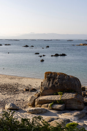 A rocky beach with a large rock in the foreground. The ocean is calm and the sky is clearの写真素材