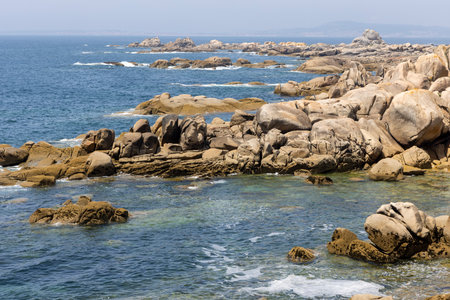 A rocky shoreline with a calm ocean in the background. The rocks are scattered across the beach, creating a rugged and natural landscape. Concept of tranquility and serenityの写真素材