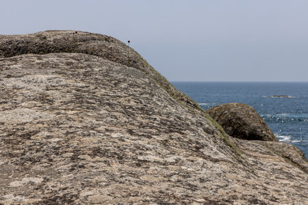A rocky hillside overlooking the ocean. The rocks are large and jagged, and the ocean is calmの写真素材