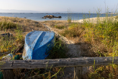 A blue boat is sitting on the beach next to a wooden bench. The scene is peaceful and serene, with the ocean in the background and the boat and bench adding to the calm atmosphereの写真素材