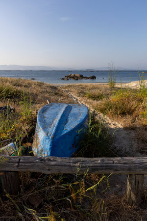 A blue boat is sitting on the beach next to a wooden bench. The scene is peaceful and serene, with the ocean in the background and the boat and bench adding to the calm atmosphereの写真素材