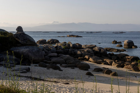 A rocky beach with a large rock in the foreground. The beach is empty and the sky is cloudyの写真素材