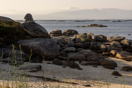 A rocky beach with a large rock in the foreground and mussels farms in background The beach is empty and the sky is cloudyの写真素材